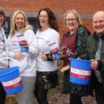 Five smiling members of the Fundraising team at Katharine House Hospice (Stafford) holding donations tins and buckets.