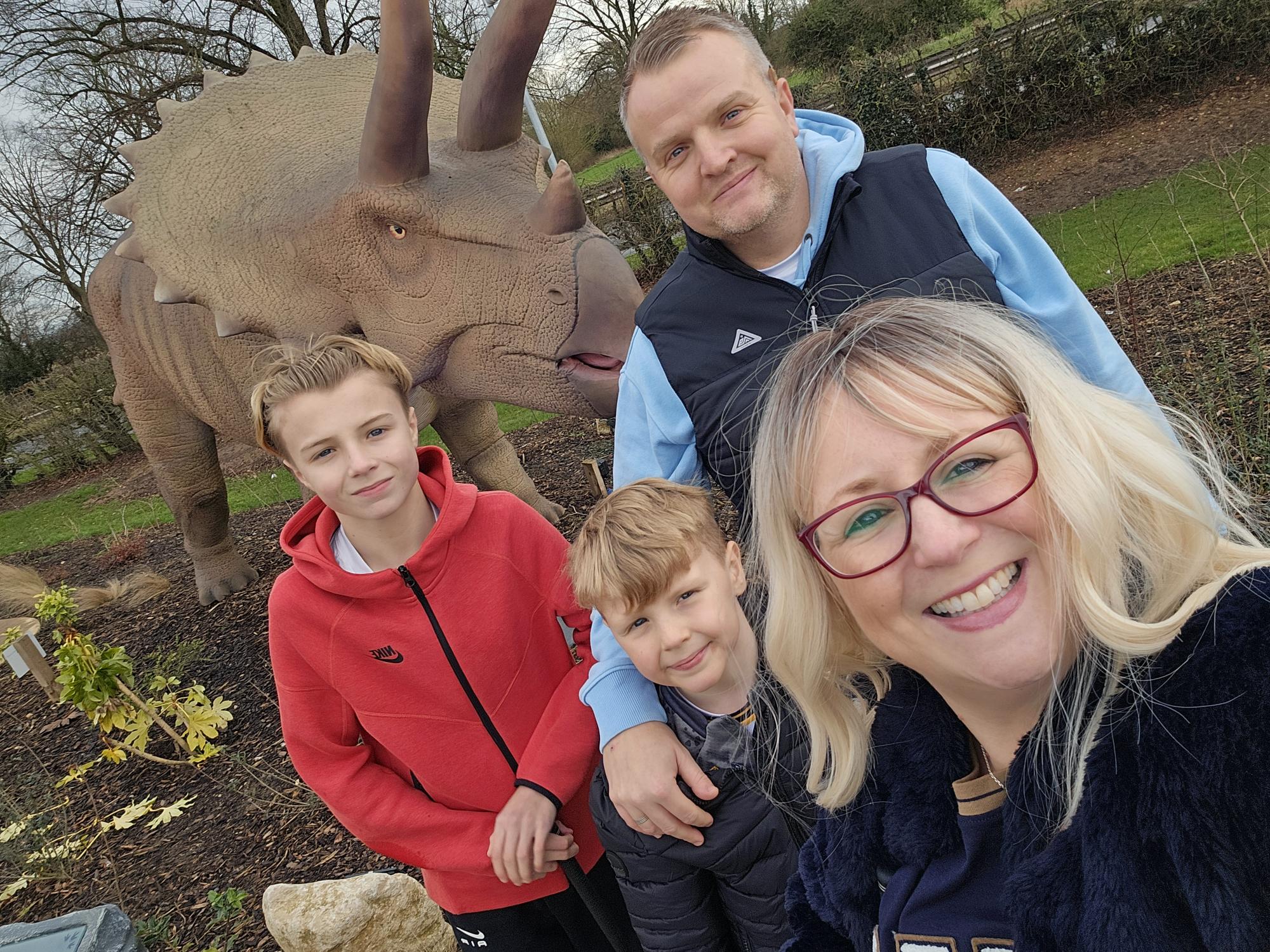 Two sons and their parents smile stood next to a dinosaur statue