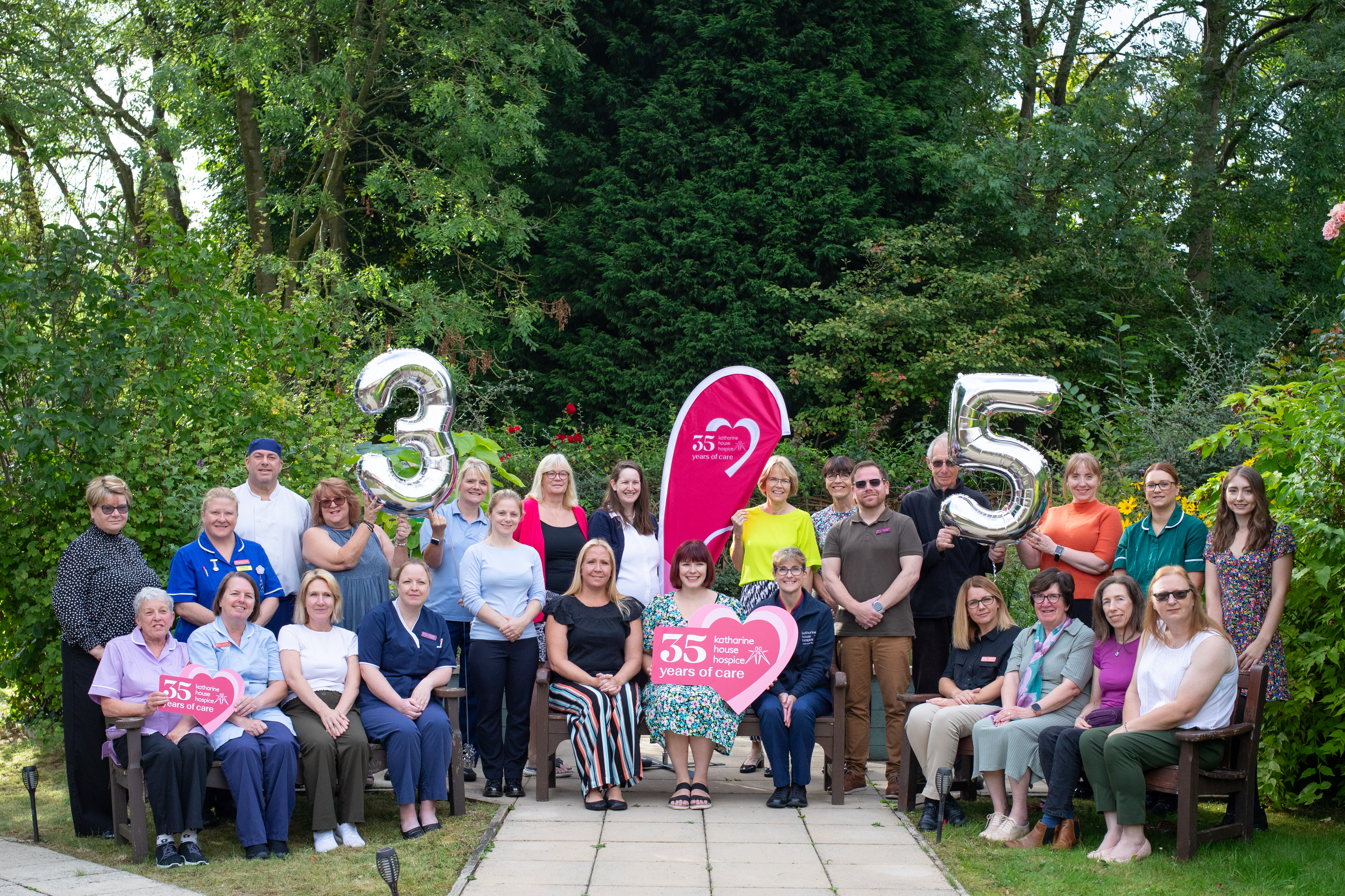 Staff at Katharine House Hospice gathering in the gardens holding balloons and signs celebrating the Hospice's 35th anniversary.