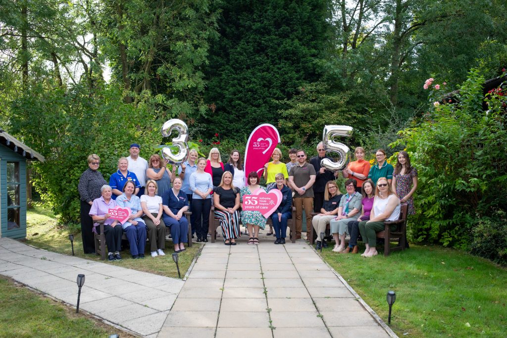 Hospice team photo in the gardens, holding up '35' balloons and props.