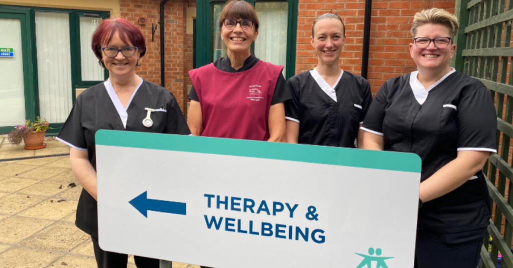 four members of the complementary therapy team standing outside the Therapy & Wellbeing Centre behind the main sign