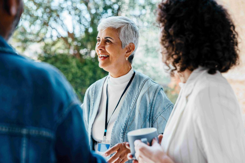 Two ladies chatting with a mug of tea A third person standing with their back to the camera