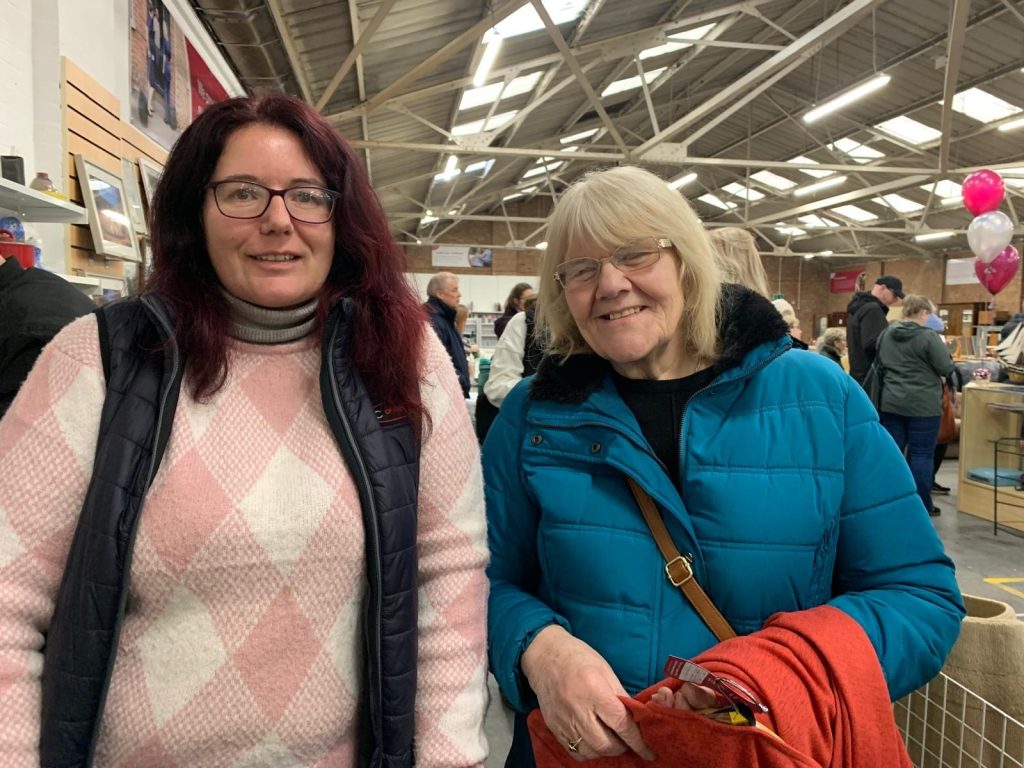 A lady in a pink jumper standing next to another older lady in a blue coat inside the shop