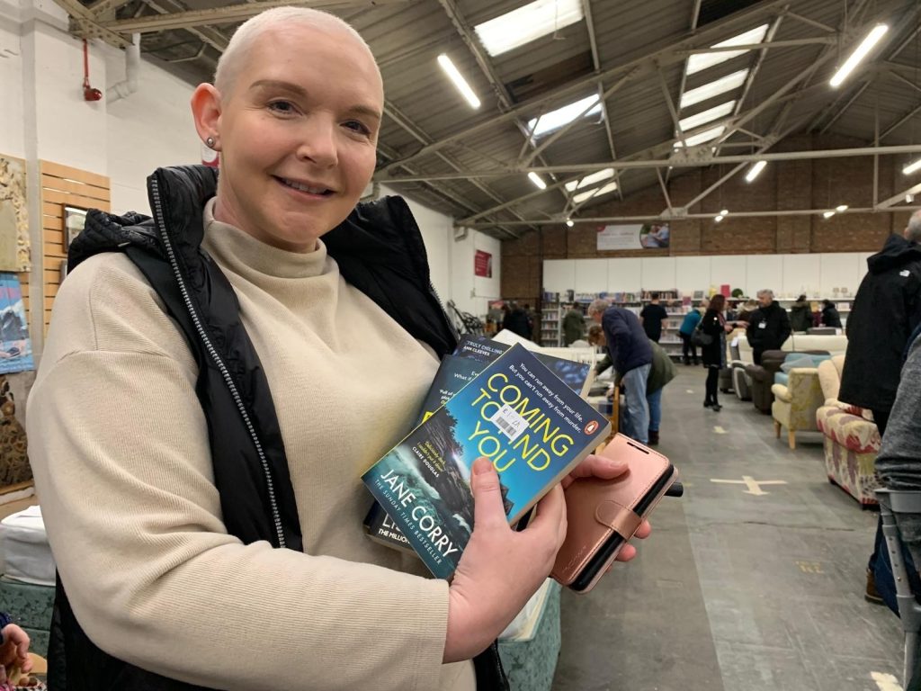 Lady wearing cream jumper and black body warmer holding up some books